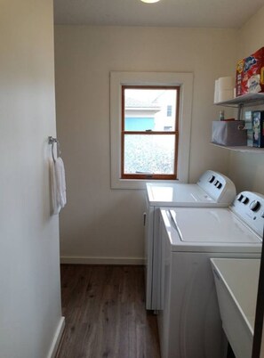 A laundry room with a washing machine and dryer, a window, and a shelf with laundry supplies.