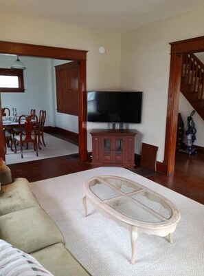 A living room with a wooden coffee table, a TV on a stand, a dining area with chairs and a table, and a staircase.