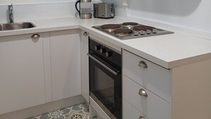 A compact kitchen with white cabinetry, a gas stove, a coffee maker, and a potted plant on the wall. - European Apartment in New Plymouth Central (New Plymouth)