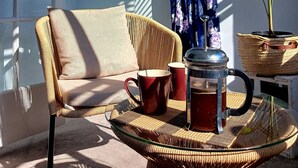 A wicker chair with a cushion, a red mug, and a metal coffee pot on a glass table. - European Apartment in New Plymouth Central (New Plymouth)
