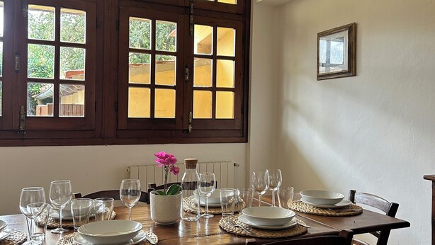 Comedor con una mesa de madera dispuesta para seis personas, rodeado de sillas de mimbre.