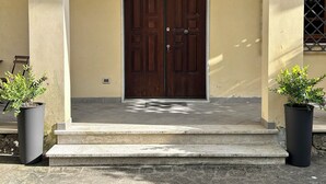 Una doble puerta de madera con un tirador de metal, flanqueada por dos faroles en la pared, que da acceso a un tramo de escalones de piedra.