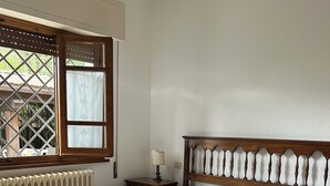 Un dormitorio con estructura de cama de madera, un radiador, una mesita de noche y una ventana con vistas a zonas verdes.