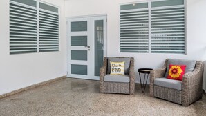 A room with a door, two wicker chairs, and a small table. - Luquillo Family Home | Sleeps 10 | Near Beach (Juan Martín)