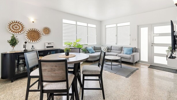 A modern living room with a dining area, a gray sofa, and a black entertainment unit. - Luquillo Family Home | Sleeps 10 | Near Beach (Juan Martín)