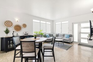 A modern living room with a dining area, a gray sofa, and a black entertainment unit. - Luquillo Family Home | Sleeps 10 | Near Beach (Juan Martín)