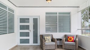 A balcony with two wicker chairs, one with a pillow that says "Be KIND" and another with a red and yellow flower pillow. - Luquillo Family Home | Sleeps 10 | Near Beach (Juan Martín)