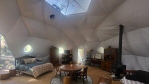 A cozy, round dining table surrounded by chairs in a tent-like interior with a bed, a wooden cabinet, and a fireplace. - Fieldbrook Gnome Dome (McKinleyville)
