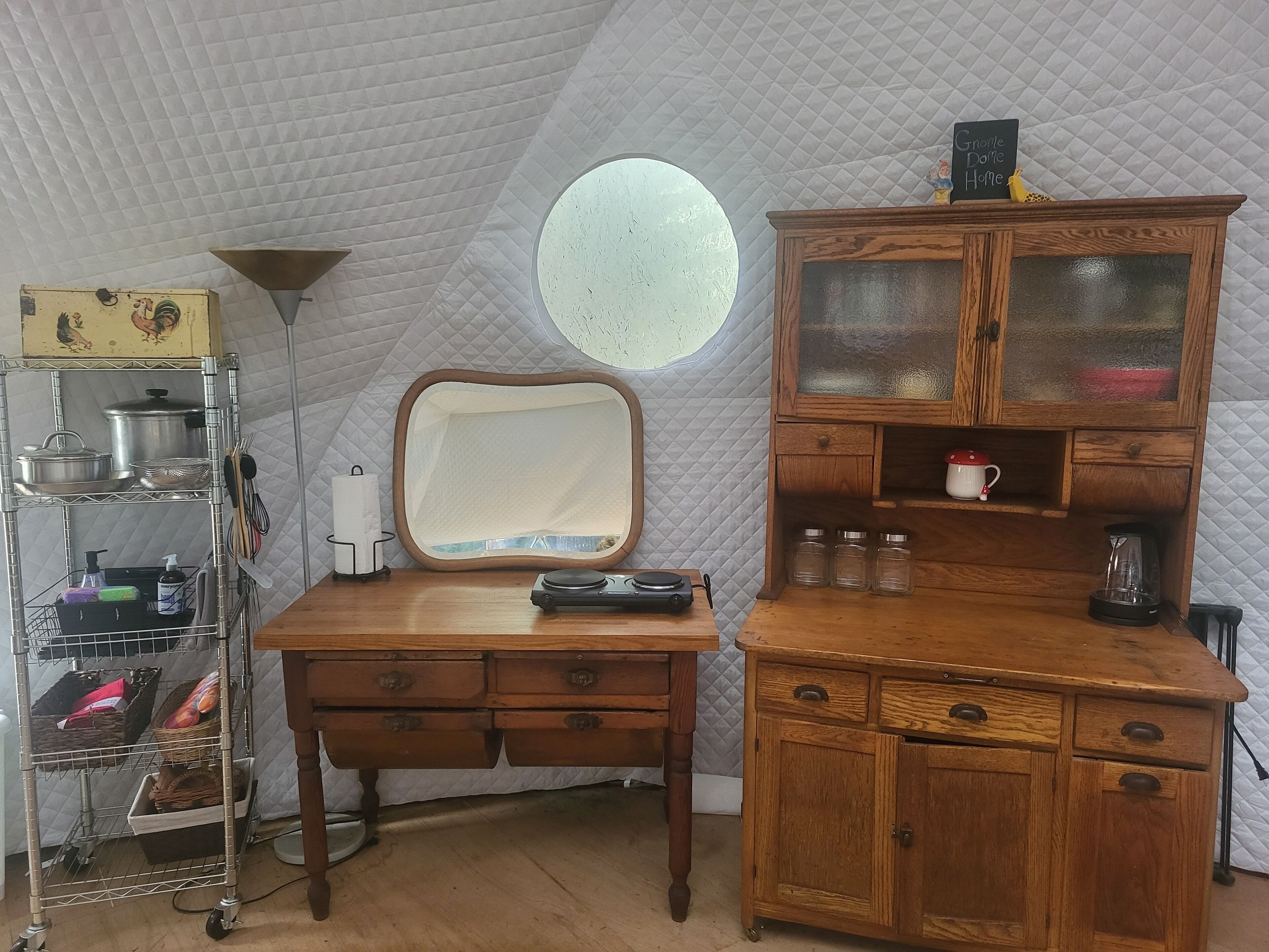 A compact, cozy room with a wooden desk, a mirror, and a cabinet with glass doors.