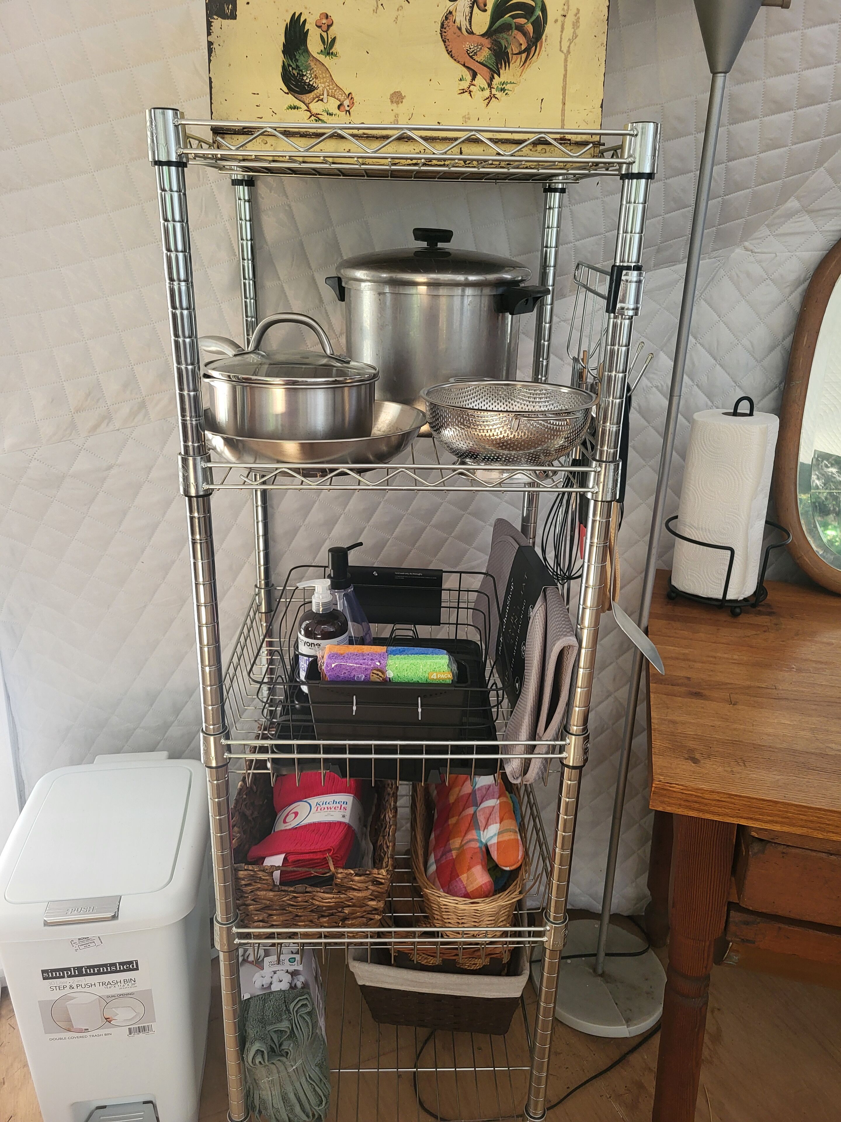 Uno scaffale in cucina con pentole, un colino, un espositore per piatti e un cestino.