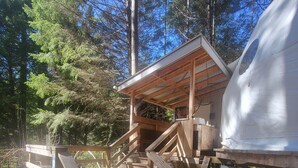 A wooden deck leading to a covered area with a view of a forest. - Fieldbrook Gnome Dome (McKinleyville)