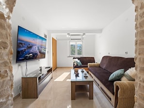 A living room with a flat-screen TV, a wooden coffee table, a brown sofa, and a stone wall.