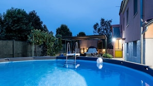 A swimming pool with a ladder, a covered seating area, and a building with a yellow door in the background. - Apartment in Vodnjan With Pool & Jacuzzi (Vodnjan)