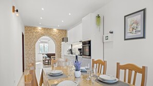 A dining area with a long table set for four, a kitchen in the background, and a stone wall. - Apartment in Vodnjan With Pool & Jacuzzi (Vodnjan)