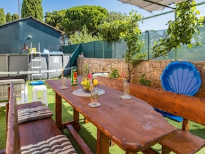 An outdoor patio with a wooden table set for dining, surrounded by a stone wall and a blue chair.