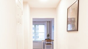 A hallway with a wooden floor, white walls, a white door, and a white bench with a vase of flowers.