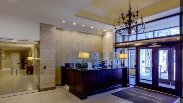 A lobby with a reception desk, a chandelier, and a glass door entrance.