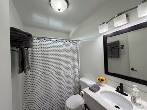 A bathroom with a striped shower curtain, a toilet, a sink with a mirror, and a towel rack. - Cozy 2-bedroom condo with WiFi, AC in lovely Lake Forest. (Lake Forest)