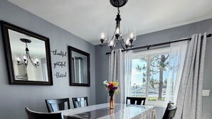 Une salle à manger avec une table, des chaises, un lustre, un vase de fleurs et une fenêtre avec des rideaux.