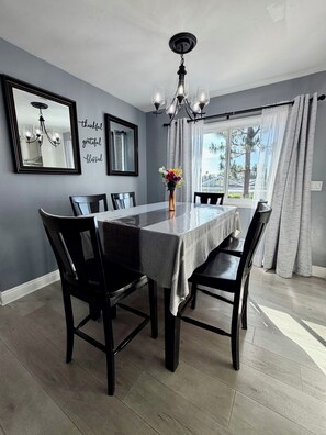 A dining room with a table, chairs, a chandelier, a vase with flowers, and a window with curtains.