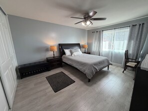 A bedroom with a bed, two bedside tables with lamps, a ceiling fan, a window with curtains, and a chair. - Cozy 2-bedroom condo with WiFi, AC in lovely Lake Forest. (Lake Forest)