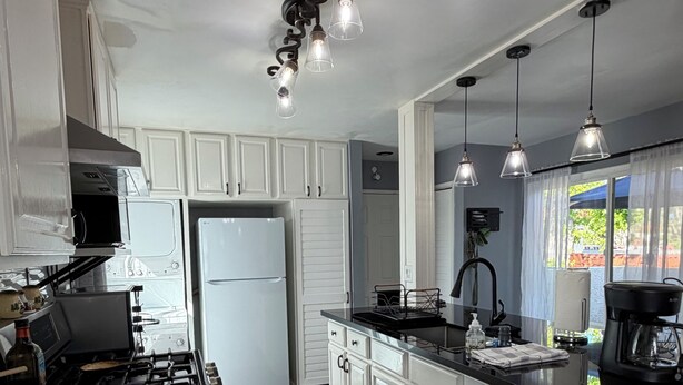 Una cocina moderna con armarios blancos, encimera negra, estufa a gas, refrigerador e iluminación colgante.
