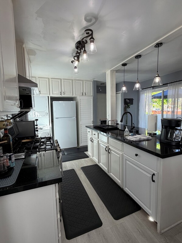 A modern kitchen with white cabinets, a black countertop, a gas stove, a refrigerator, and pendant lighting. - Cozy 2-bedroom condo with WiFi, AC in lovely Lake Forest. (Lake Forest)