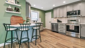 Une cuisine moderne dotée d’un coin bar, d’appareils électroménagers en acier inoxydable et d’un dosseret en carreaux disposés en motif chevrons.