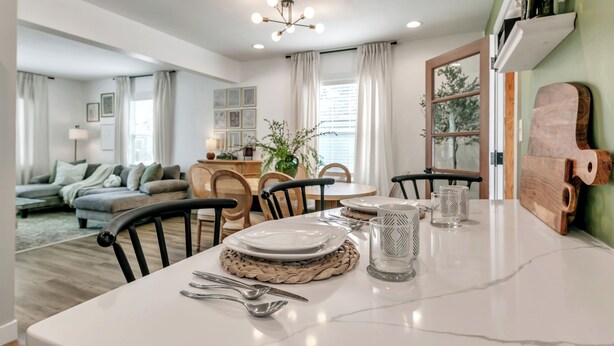 Un coin repas avec une table blanche dressée pour quatre personnes, entourée de chaises, et un jeu de société en bois posé sur la table.