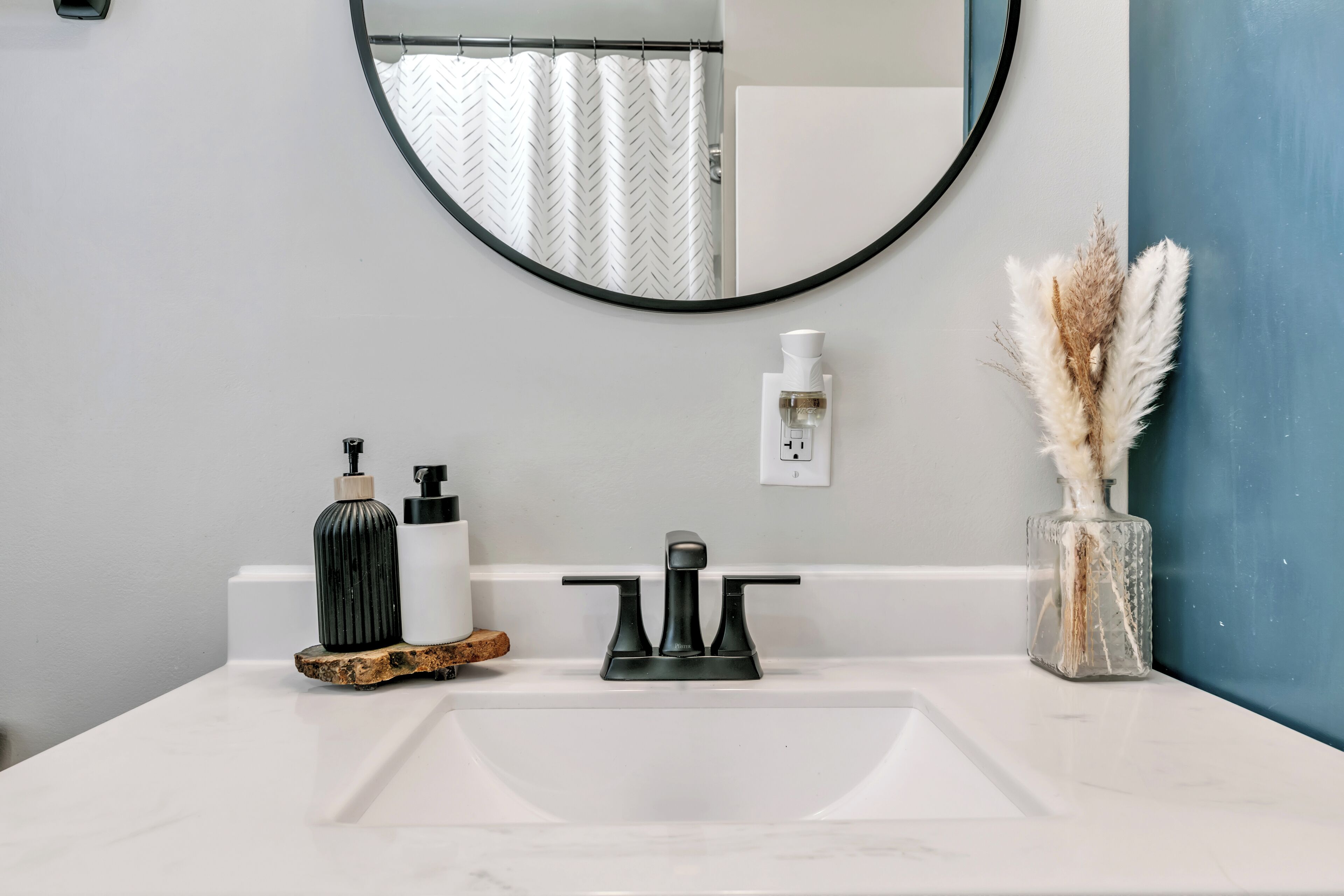 A bathroom with a white sink, a black faucet, a mirror, and a vase with dried pampas grass.
