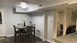 Een eetruimte met een tafel en stoelen, een vaas met bloemen en een plafondlamp.