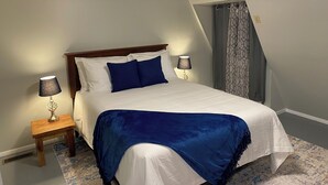 Een net opgemaakt bed met een houten hoofdbord, twee bedlampen en een blauwe plaid.