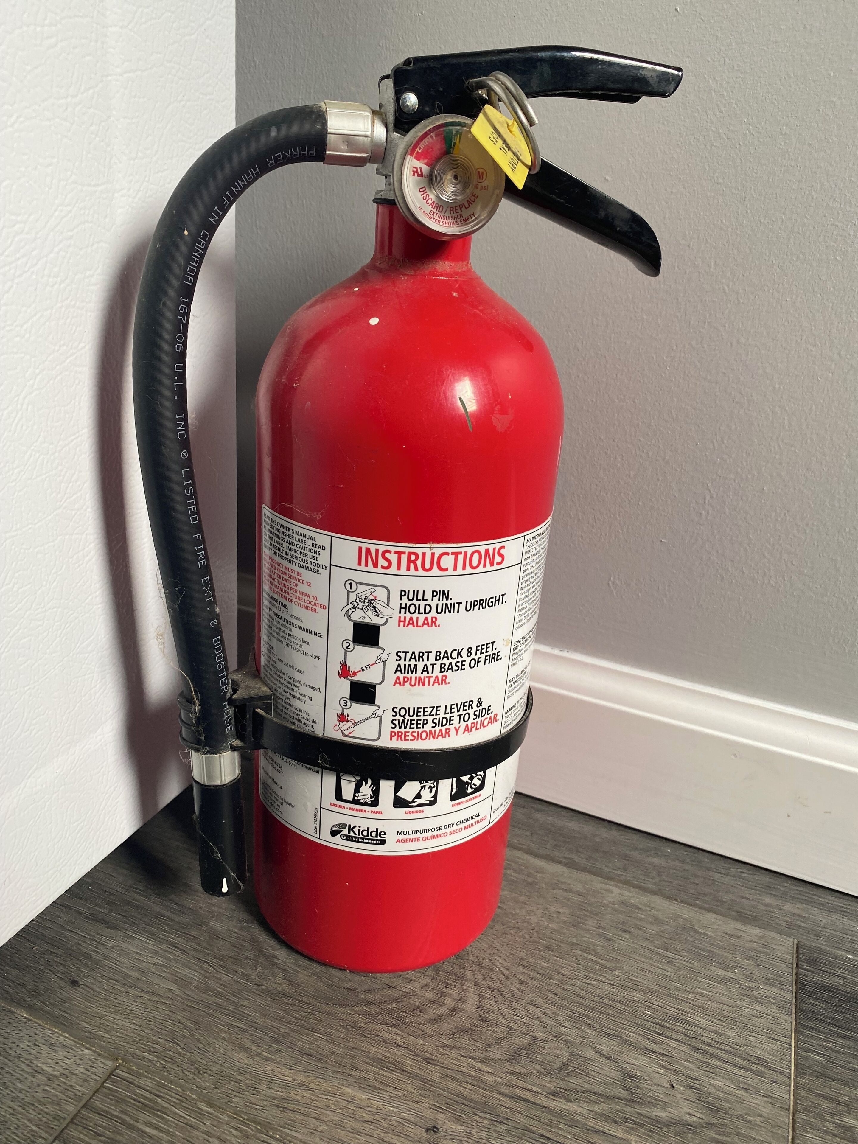A red fire extinguisher mounted on a wall next to a wooden floor.