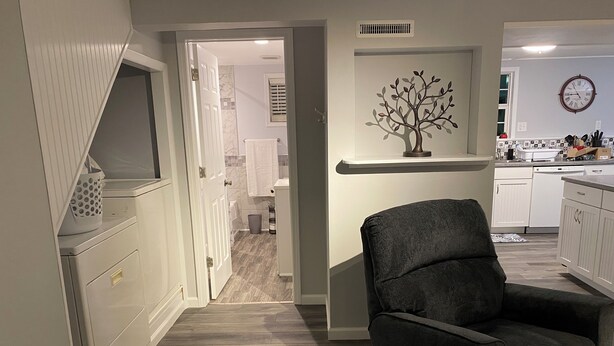 Een moderne keuken met witte kastjes, een donkergrijze fauteuil en een decoratief kunstwerk van een boom aan de muur.