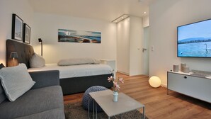 A modern, well-lit living room with a sofa, a bed, a TV, and a painting on the wall. - Domizil Strandallee 30 Apartment 8, Casa Bolz - Domizil Strandallee 30 (Timmendorfer Strand)