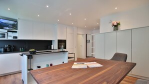 A modern kitchen with white cabinetry, a wooden dining table, and a view of the sea through a window. - Domizil Strandallee 30 Apartment 8, Casa Bolz - Domizil Strandallee 30 (Timmendorfer Strand)