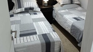 Una habitación pequeña y tenue, con dos camas, una mesita de noche con lámpara y una ventana con cortinas.