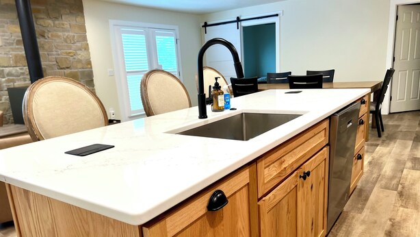 Una cocina con una isla grande, armarios de madera, un lavamanos de acero inoxidable y un grifo negro.