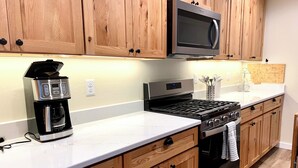 Una cocina con armarios de madera, microondas de acero inoxidable, cafetera y estufa a gas.