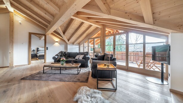 A spacious living room with wooden beams, a large window, a sofa, a coffee table, and a TV.