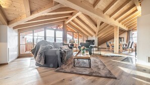 A spacious loft with high ceilings, wooden beams, and large windows offering views of the outdoors.