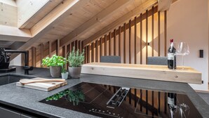 A modern kitchen with a black induction cooktop, wooden beams, and potted plants.