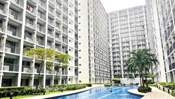 Un edifici d'apartaments modern amb piscina, envoltat de vegetació i palmeres.