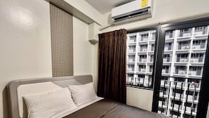 Habitació d'hotel amb llit, aire condicionat, finestra amb cortines i vista a un edifici amb balcons.