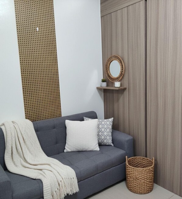 A grey sofa with a white throw blanket, a patterned pillow, and a woven basket. - Mall of Asia - Aseana Prime Accommodations (Pasay)