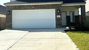 A two-story house with a white garage door, a brick facade, and a small front porch. - Master Bedroom with Private Bathroom (Houston)