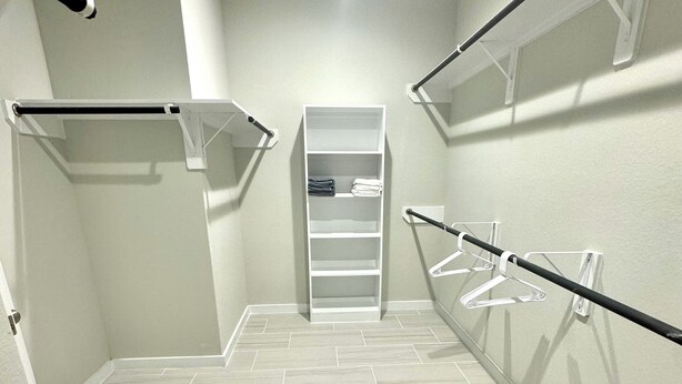 A walk-in closet with a white shelving unit, metal hangers, and a tiled floor. - Master Bedroom with Private Bathroom (Houston)
