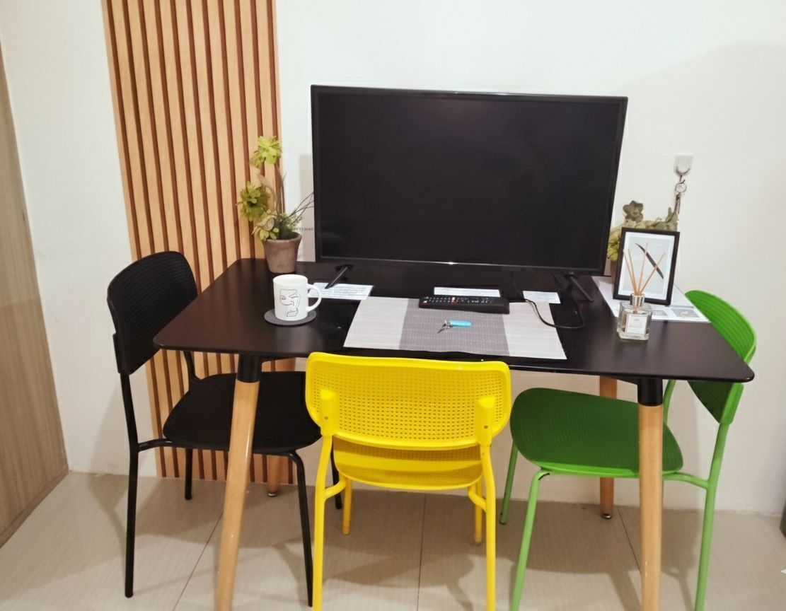 A room with a large flat-screen TV, a wooden partition, two chairs, a small table, and a potted plant.