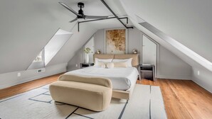 Una camera da letto moderna con soffitto a falde, un letto con struttura in legno, una panca imbottita color beige e una ventola a soffitto.