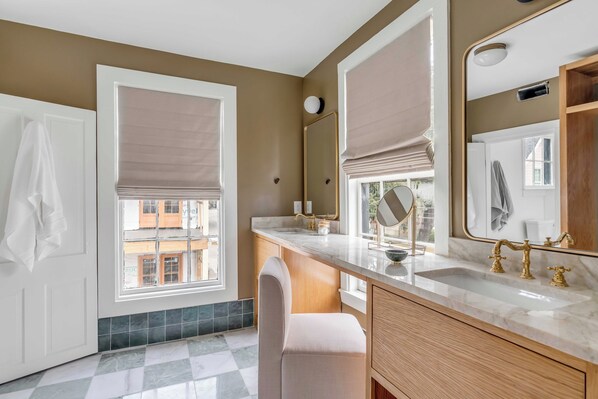 A modern bathroom with a large mirror, a sink with gold fixtures, and a checkered floor. - Emerson Square (Charleston)